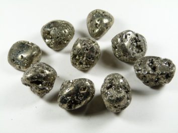 Piryt - kamień gładzony, polerowany, szlifowany i bębnowany w formie otoczaka. Dziewięć bryłek pirytu o metalicznym połysku ułożonych na białym tle.