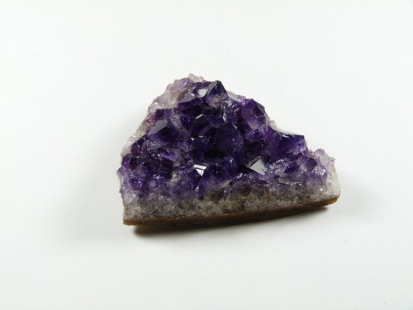 Trójkątny kawałek ametystu z fioletowymi kryształami na białym tle.