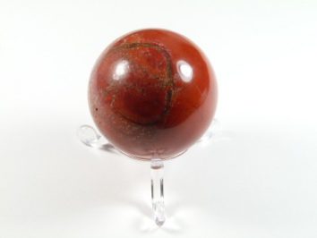 Kula jaspis czerwony na podstawce. Czerwona, polerowana kula z jaspisu na przezroczystej podstawce, na białym tle.