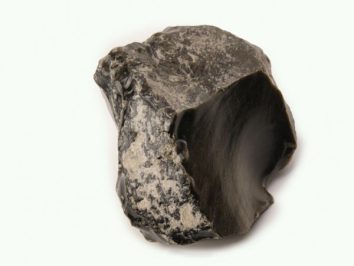 Czarny, połyskujący kawałek obsydianu na jasnym tle.