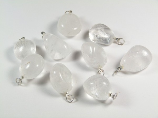 Osiem przezroczystych kamieni z metalowymi zawieszkami leży na białym tle.