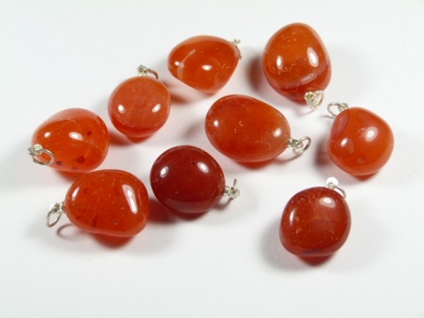 Dziewięć czerwonych kamieni z oczkami do zawieszenia, ułożonych na białym tle.