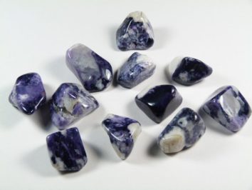 Kilka fioletowo-białych, oszlifowanych kamieni leży na białym tle.