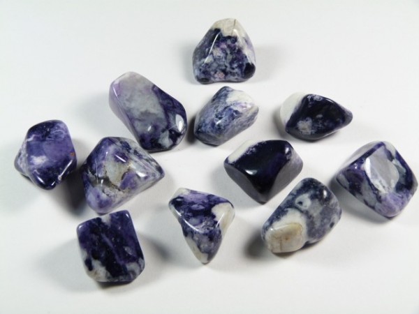Kilka fioletowo-białych, oszlifowanych kamieni leży na białym tle.