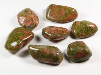 Siedem wypolerowanych kamieni o zielono-czerwonych wzorach leży na białym tle.