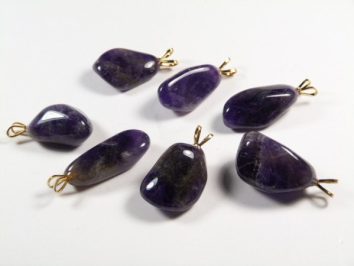 Siedem fioletowych zawieszek z kamieniami ametystu na białym tle.
