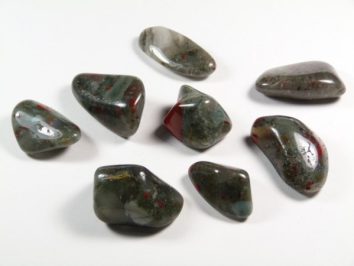 Osiem wypolerowanych kamieni jaspisu w różnych odcieniach zieleni z czerwonymi plamkami.