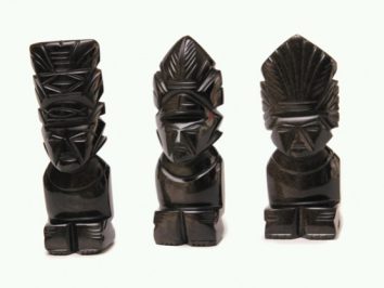 Trzy czarne, rzeźbione figurki siedzących postaci o geometrycznych twarzach i ozdobnych nakryciach głowy.