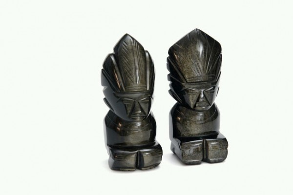 Dwie czarne figurki przedstawiające postacie z pióropuszami na głowie, ustawione obok siebie.