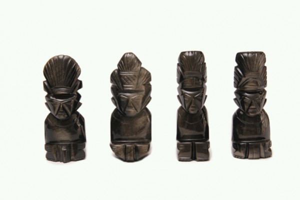 Cztery czarne figurki przedstawiające stylizowane postaci z pióropuszami ustawione w rzędzie.