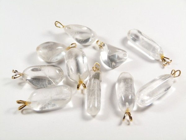 Kilka przezroczystych wisiorków z kryształu górskiego leży na białym tle.
