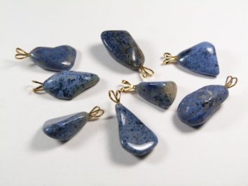Osiem niebieskich kamieni z zawieszkami, ułożonych na białym tle.