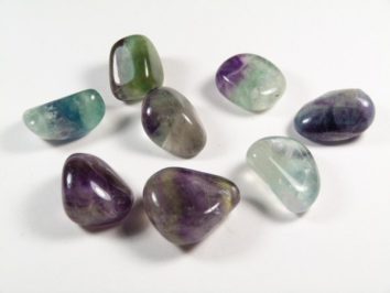 Osiem wypolerowanych, kolorowych kamieni fluorytu leży na białym tle.