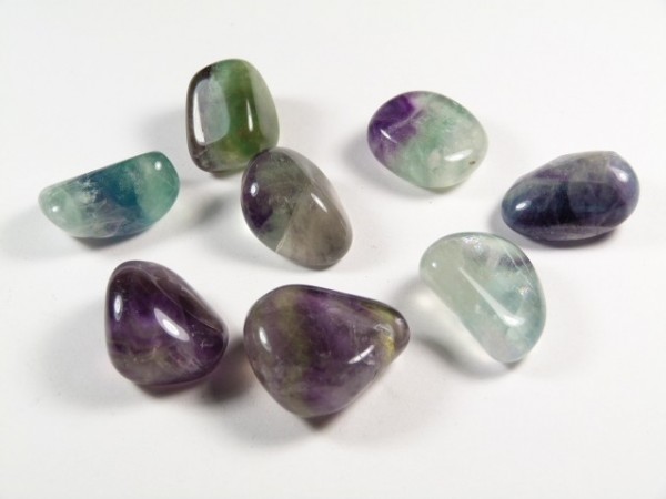 Osiem wypolerowanych, kolorowych kamieni fluorytu leży na białym tle.