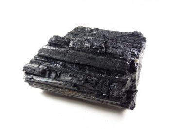 Czarny minerał turmalin o nieregularnej, błyszczącej powierzchni na białym tle.