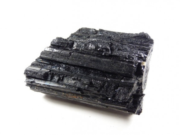 Czarny minerał turmalin o nieregularnej, błyszczącej powierzchni na białym tle.