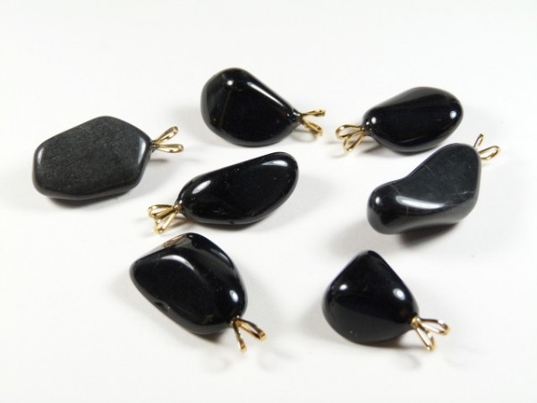 Siedem czarnych, polerowanych kamieni z metalowymi zawieszkami leży na białym tle.