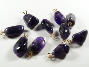 Dziesięć fioletowych zawieszek z kamieniami ametystu leży na białym tle.