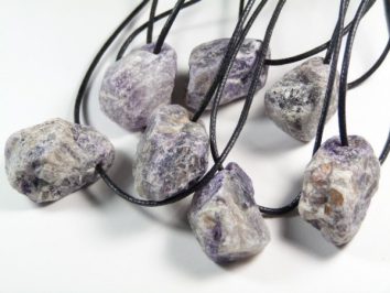 Siedem surowych kamieni na czarnych sznurkach, ułożonych na białym tle.