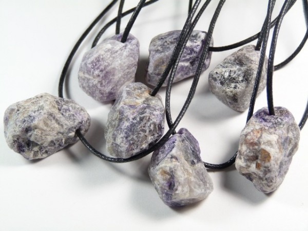 Siedem surowych kamieni na czarnych sznurkach, ułożonych na białym tle.