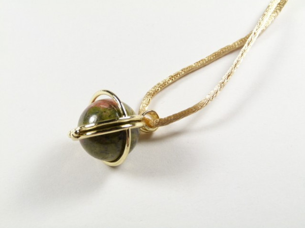 Wisiorek z zieloną kulką w złotym oplocie na złotym sznurku, leżący na białym tle.