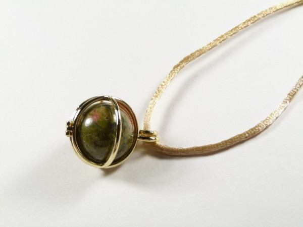 Naszyjnik z okrągłym, zielonym kamieniem w złotej oprawie na jasnym sznurku.