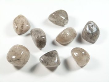 Kwarc turmalinowy - kamień gładzony, polerowany, szlifowany i bębnowany w formie otoczaka. Osiem wypolerowanych kamieni kwarcu z inkluzjami na białym tle.