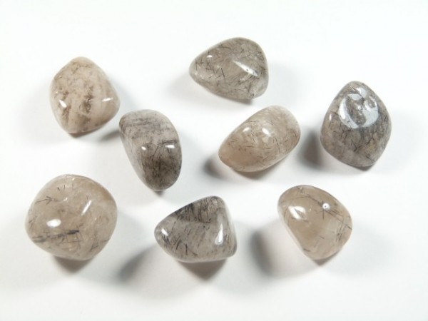 Kwarc turmalinowy - kamień gładzony, polerowany, szlifowany i bębnowany w formie otoczaka. Osiem wypolerowanych kamieni kwarcu z inkluzjami na białym tle.