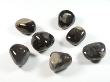 Krzemień - kamień gładzony, polerowany, szlifowany i bębnowany w formie otoczaka. Siedem wypolerowanych, ciemnych kamieni leży na białym tle.