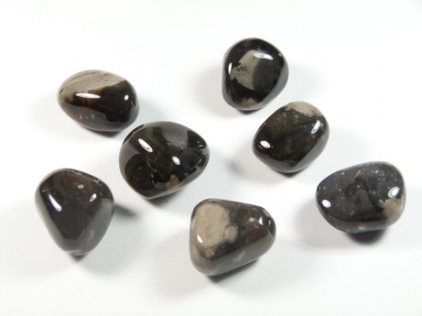 Krzemień - kamień gładzony, polerowany, szlifowany i bębnowany w formie otoczaka. Siedem wypolerowanych, ciemnych kamieni leży na białym tle.