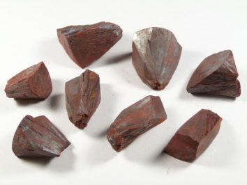 Osiem czerwono-brązowych kryształów hematytu leży na białym tle.