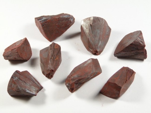 Osiem czerwono-brązowych kryształów hematytu leży na białym tle.