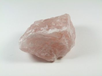Różowy, surowy kryształ kwarcu leży na białym tle.