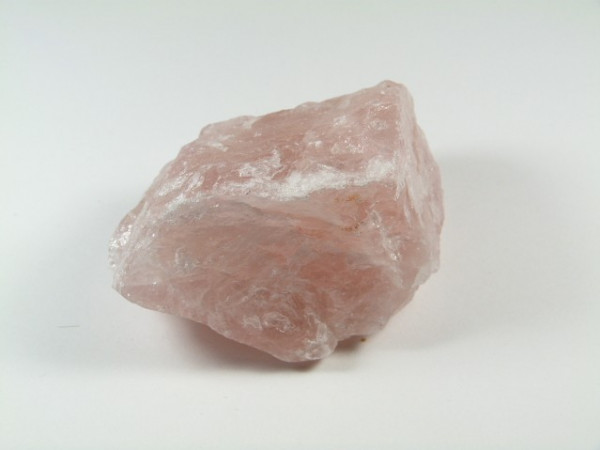 Różowy, surowy kryształ kwarcu leży na białym tle.
