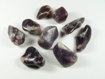 Osiem fioletowo-białych, gładkich kamieni leży na białym tle.