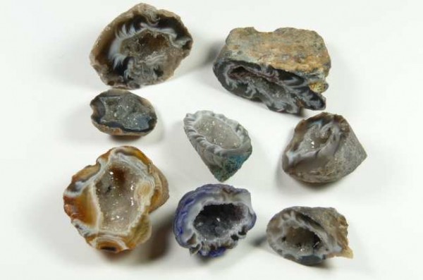 Agat mini geoda - kamień naturalny, surowy, nieszlifowany. Kilka różnych geod z widocznymi kryształami wewnątrz, ułożonych na białym tle.