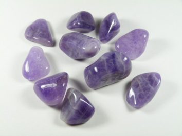 Dziesięć wypolerowanych, fioletowych kamieni ametystu na białym tle.