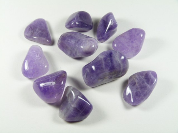 Dziesięć wypolerowanych, fioletowych kamieni ametystu na białym tle.