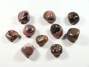Rodonit - kamień gładzony, polerowany, szlifowany i bębnowany w formie otoczaka. Dziesięć wypolerowanych kamieni o różowych i czarnych wzorach na białym tle.