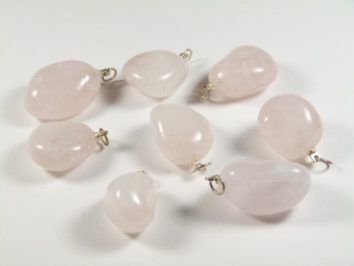 Osiem różowych, gładkich kamieni z zawieszkami do biżuterii leży na białym tle.