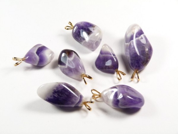 Siedem fioletowych zawieszek z kamieniami ametystu na białym tle.
