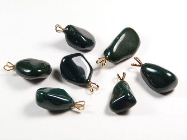 Siedem ciemnozielonych, polerowanych kamieni z metalowymi zawieszkami na białym tle.