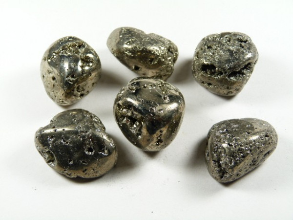 Piryt - kamień gładzony, polerowany, szlifowany i bębnowany w formie otoczaka. Sześć bryłek błyszczącego pirytu leży na białym tle.