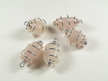 Cztery różowe kamienie owinięte srebrnym drutem, ułożone na białym tle.