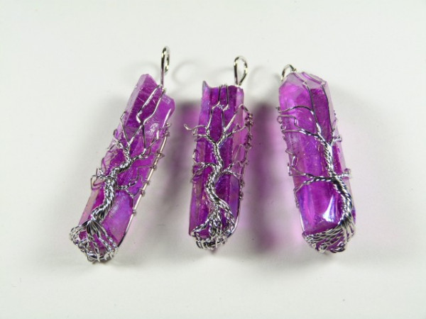 Trzy fioletowe kryształy oplecione srebrnym drutem na białym tle.