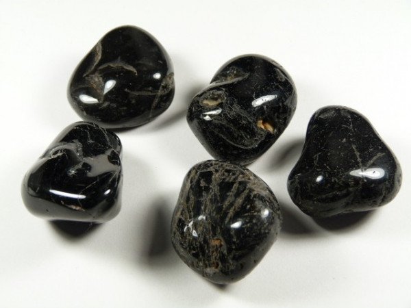 Pięć czarnych, wypolerowanych kamieni leży na białym tle.