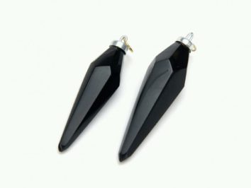 Dwa czarne, szpiczaste wisiorki z metalu, leżące na jasnym tle.