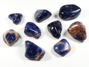 Dziewięć oszlifowanych kamieni sodalitu w niebiesko-pomarańczowym kolorze na białym tle.