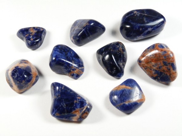 Dziewięć oszlifowanych kamieni sodalitu w niebiesko-pomarańczowym kolorze na białym tle.