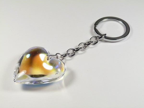 Breloczek z przezroczystym sercem na metalowym łańcuszku, leżący na białym tle.